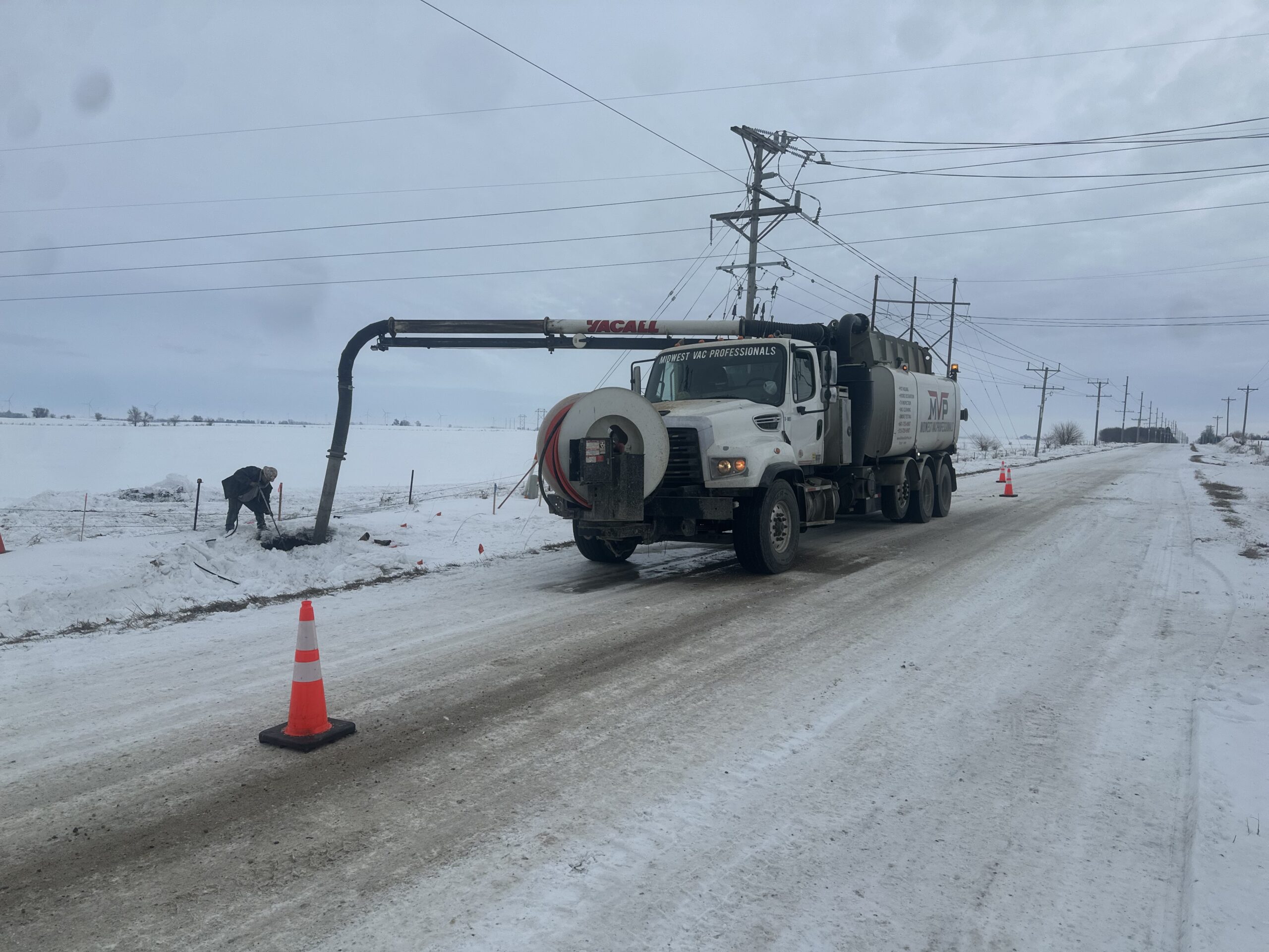 MVP vacuum truck with extended boom hose working roadside in snowy conditions, with traffic cones marking the work zone.
